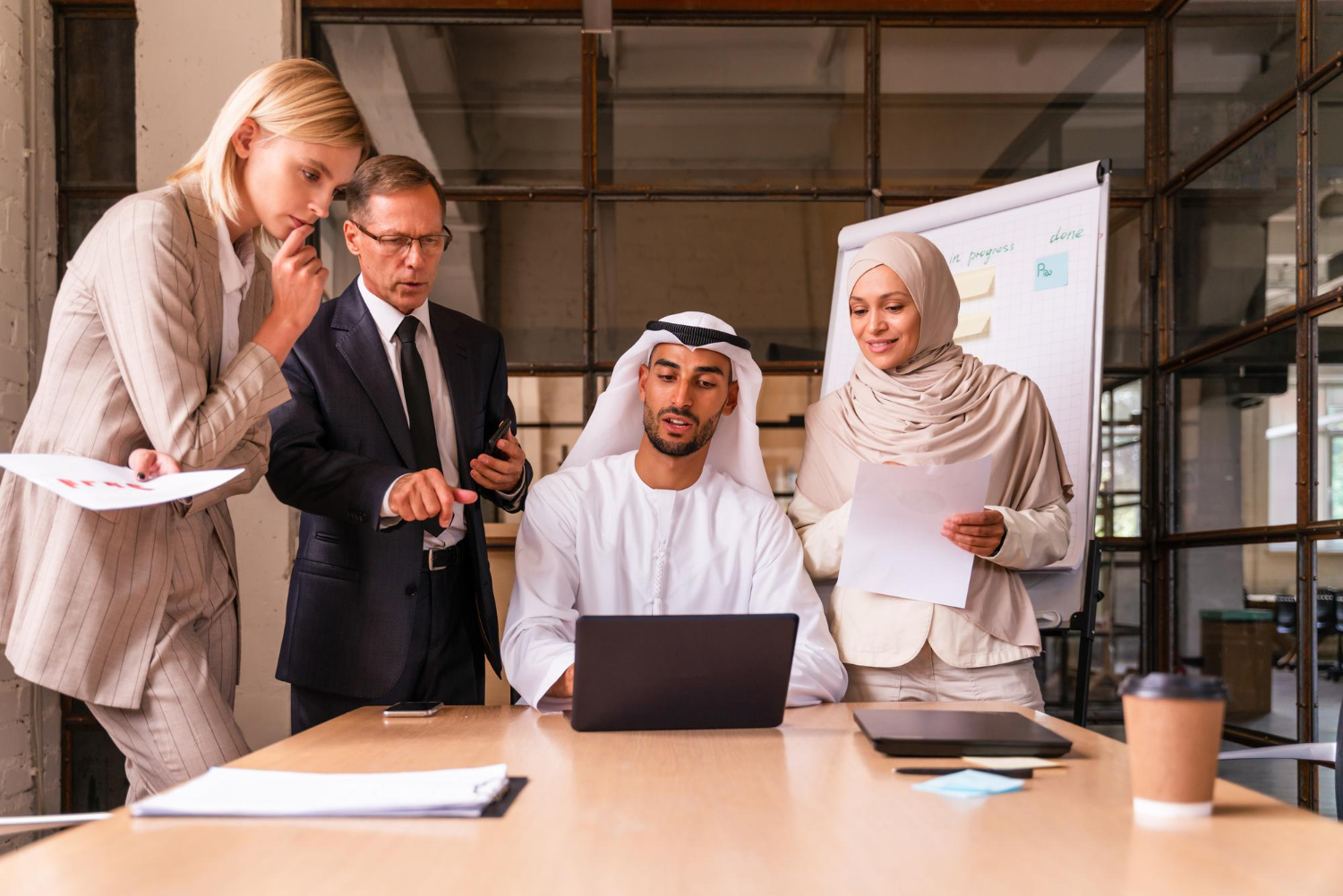 Business professionals discussing HR strategies around a laptop in a modern UAE office — ideal representation of HR Software UAE in action.
