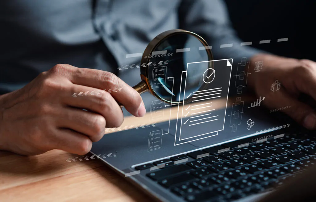 Person analyzing digital HR documents on a laptop with a magnifying glass, representing top HR & payroll solutions for businesses in the UAE.