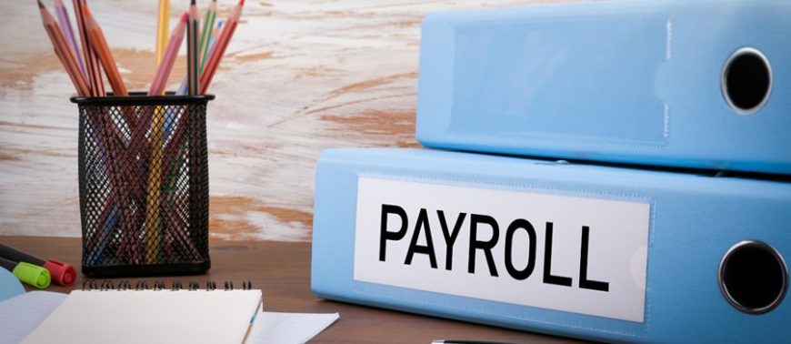 Two blue binders labeled 'Payroll' on a desk with stationery, symbolizing efficient payroll management solutions in Pakistan.