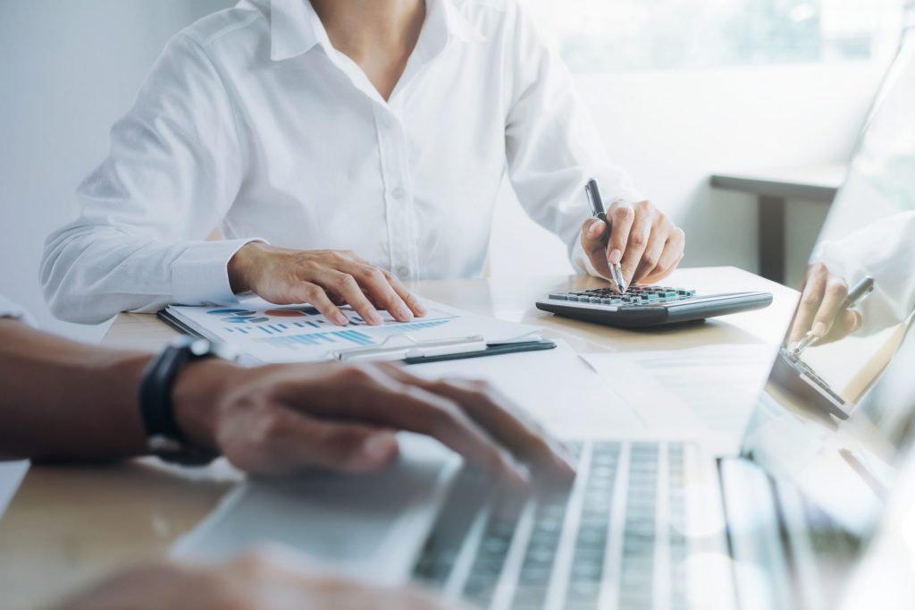 Professional accountant calculating payroll outsourcing costs and compliance benefits at modern office desk with calculator and financial reports
